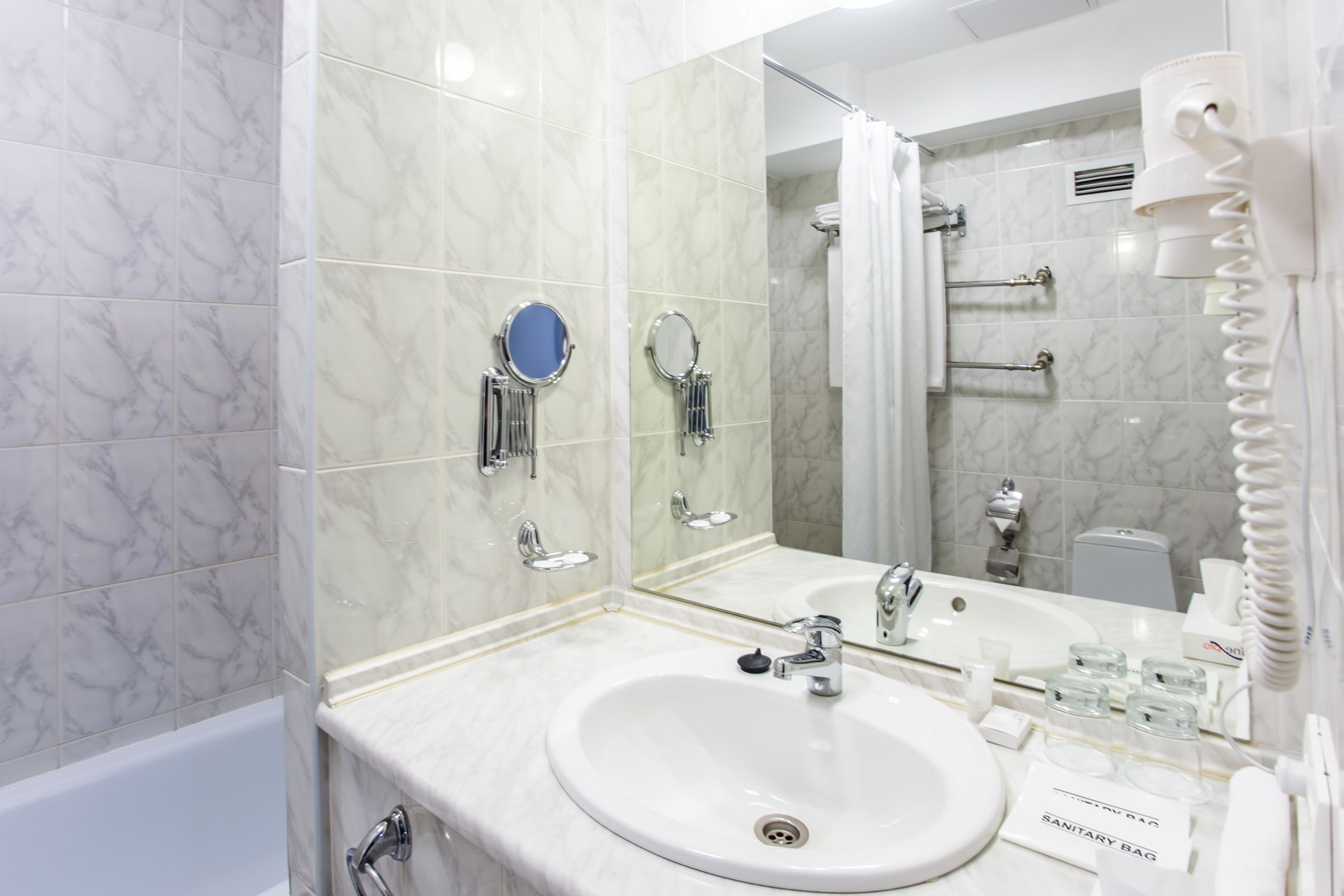A modern bathroom with a white sink, a large mirror, and a shower area.