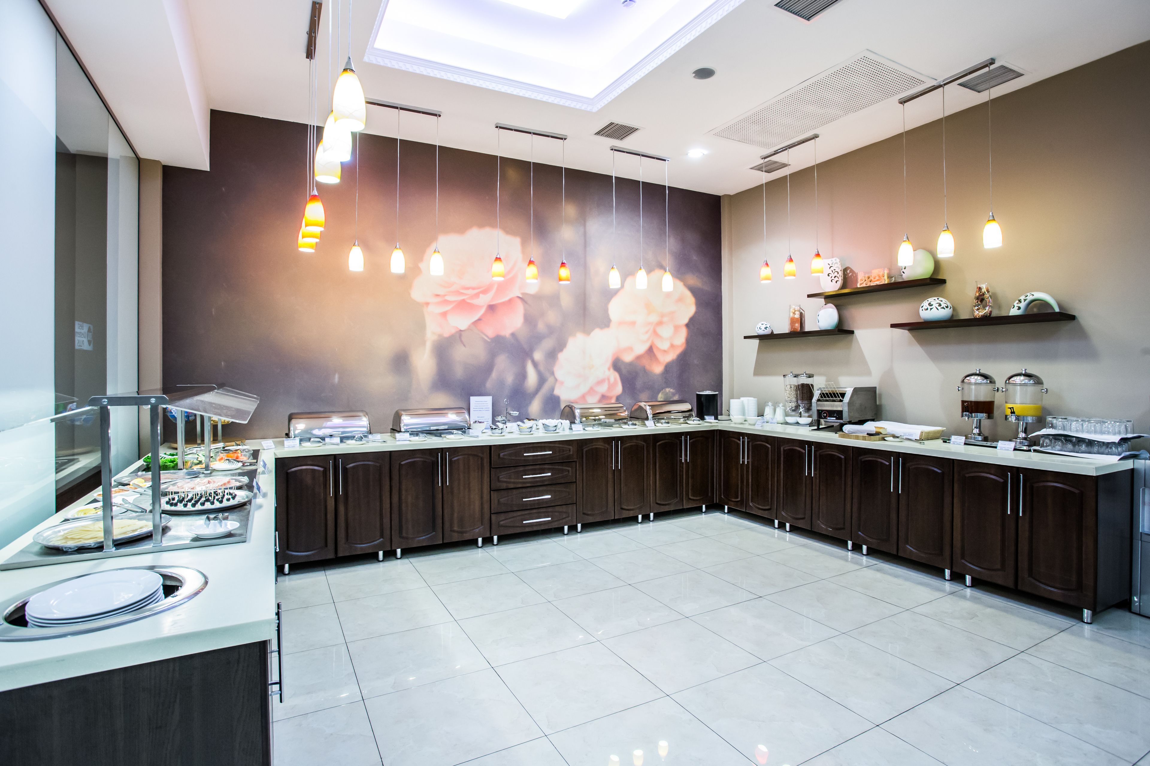 A modern kitchen with a central island, overhead pendant lights, and a floral mural on the wall.