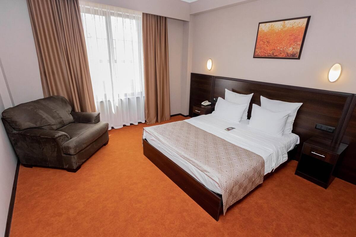 A hotel room with a large bed, a sofa, a nightstand, and a painting on the wall.