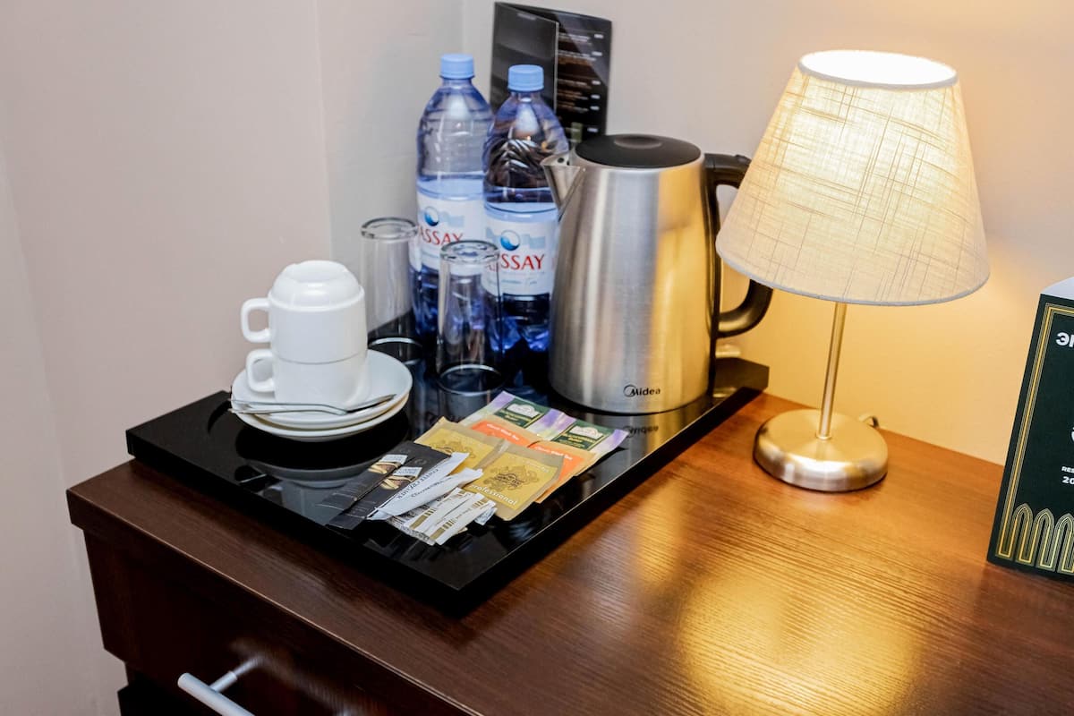 A hotel room's minibar with a coffee maker, water bottles, a coffee cup, glasses, and a lamp.