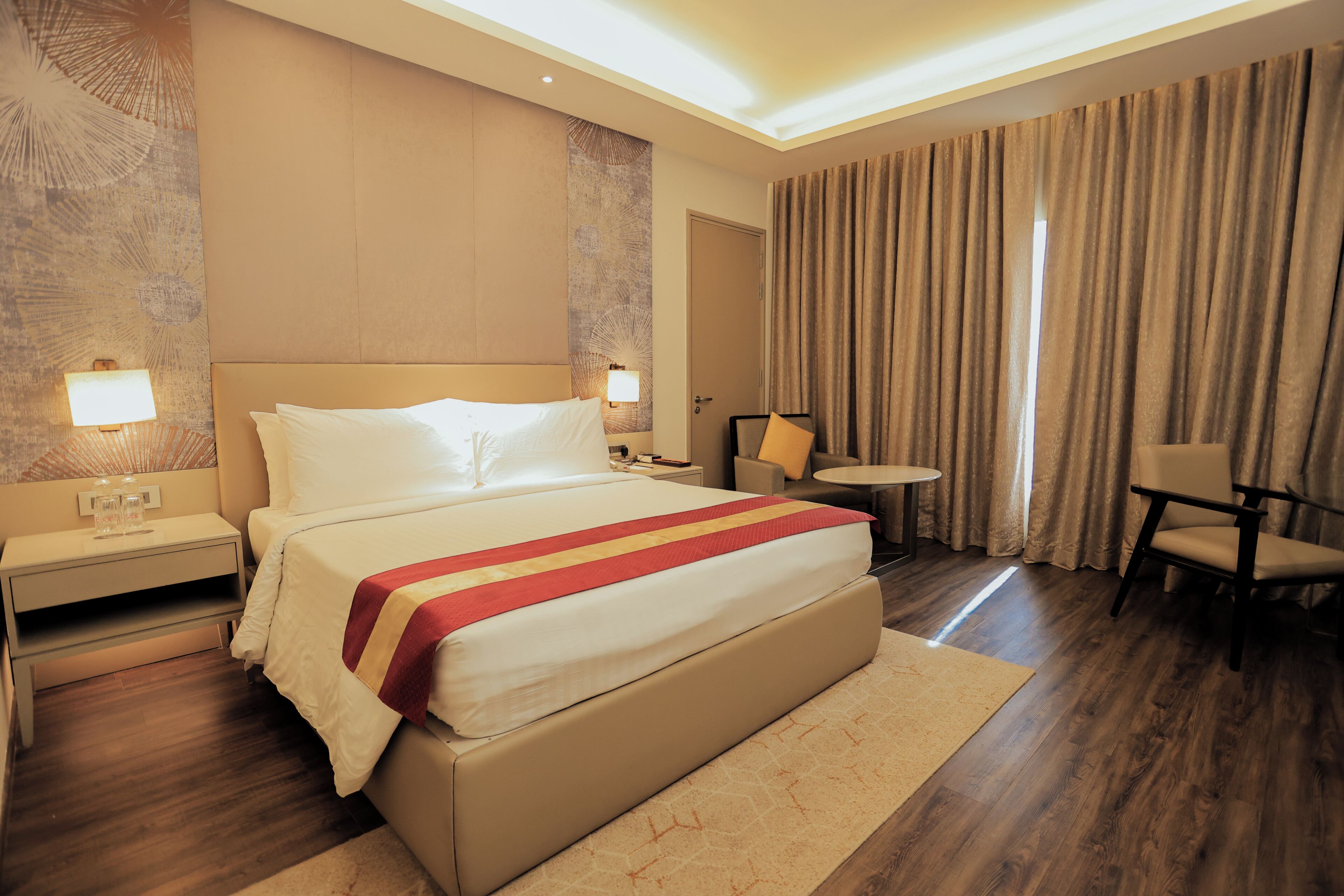 Une chambre d’hôtel avec un grand lit, des tables de chevet, une petite table ronde, une chaise et une porte.