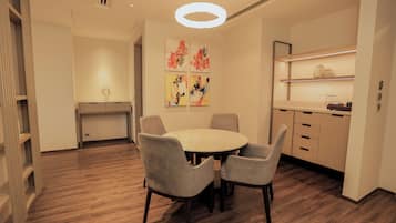 A modern dining area with a round table and four chairs, a kitchen with open shelving, and abstract wall art.