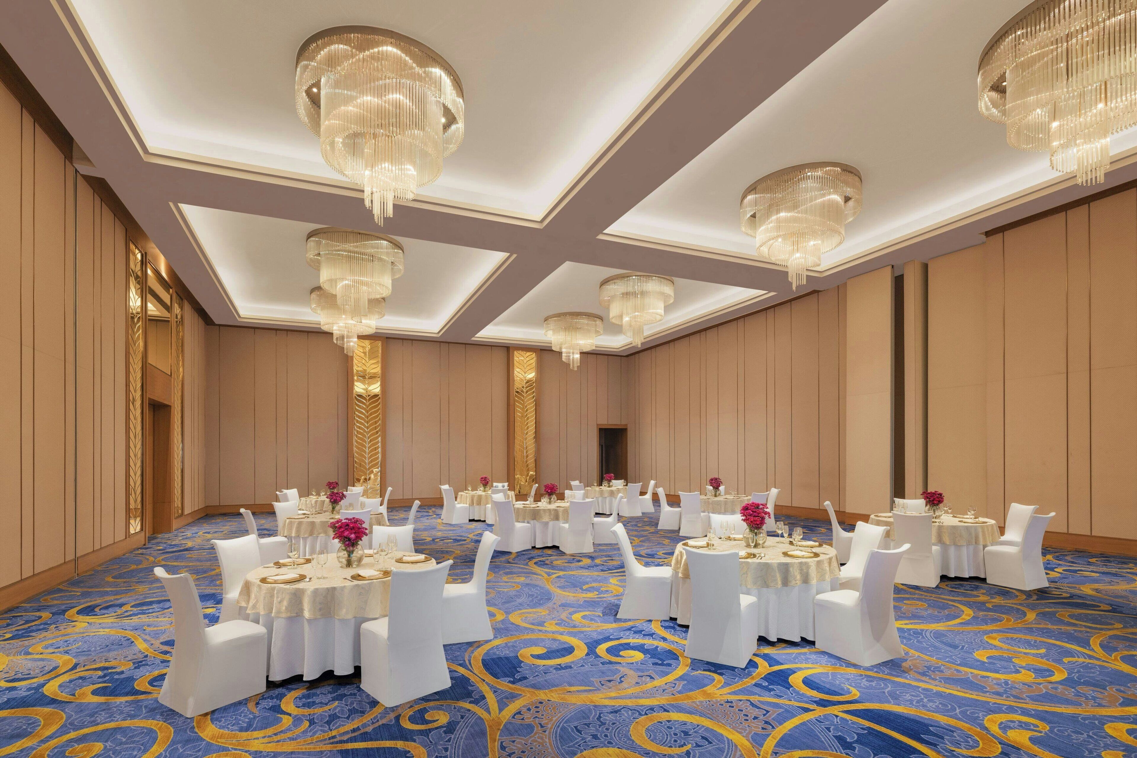A banquet hall with round tables, white chairs, and chandeliers.