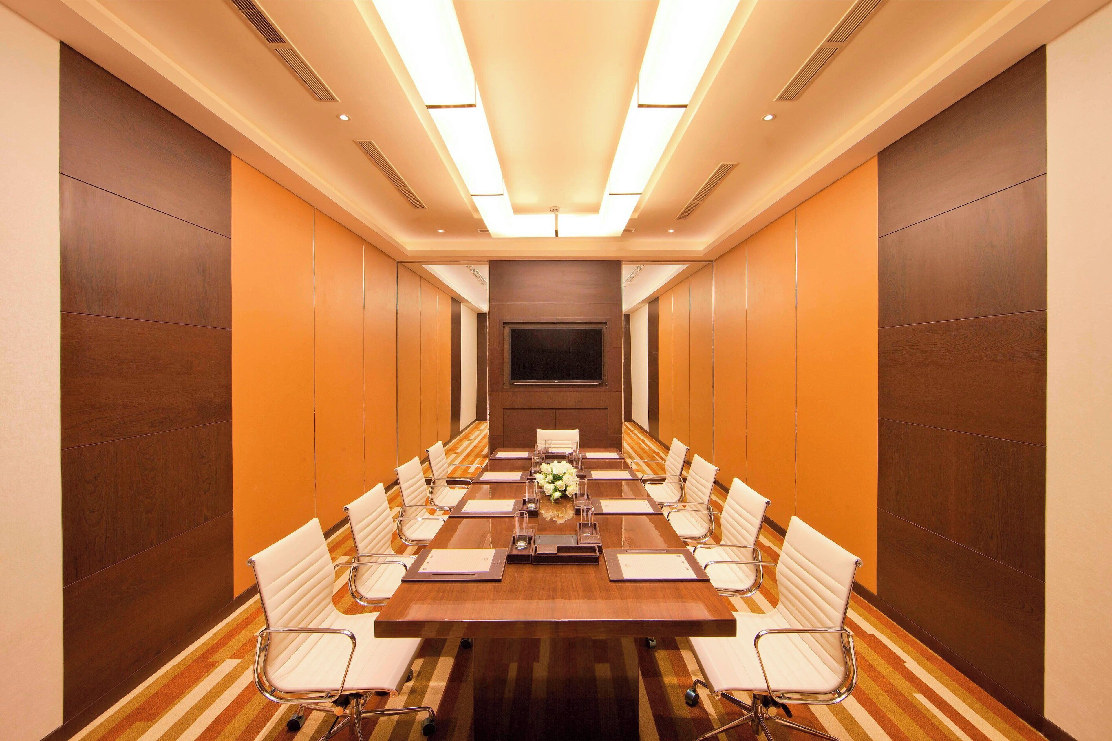A conference room with a long table, white chairs, and a floral centerpiece.