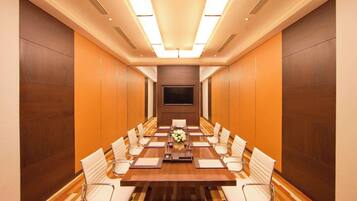 Un salón de conferencias con una mesa larga, sillas blancas y un centro de mesa floral.