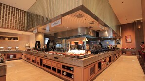 Uma área de buffet com ilha central, várias estações de serviço e teto alto com ventilação.