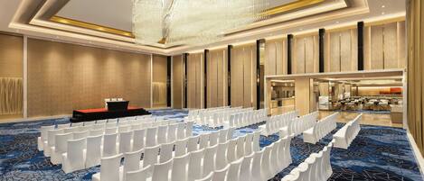 A conference room with rows of white chairs, a podium, and a chandelier.