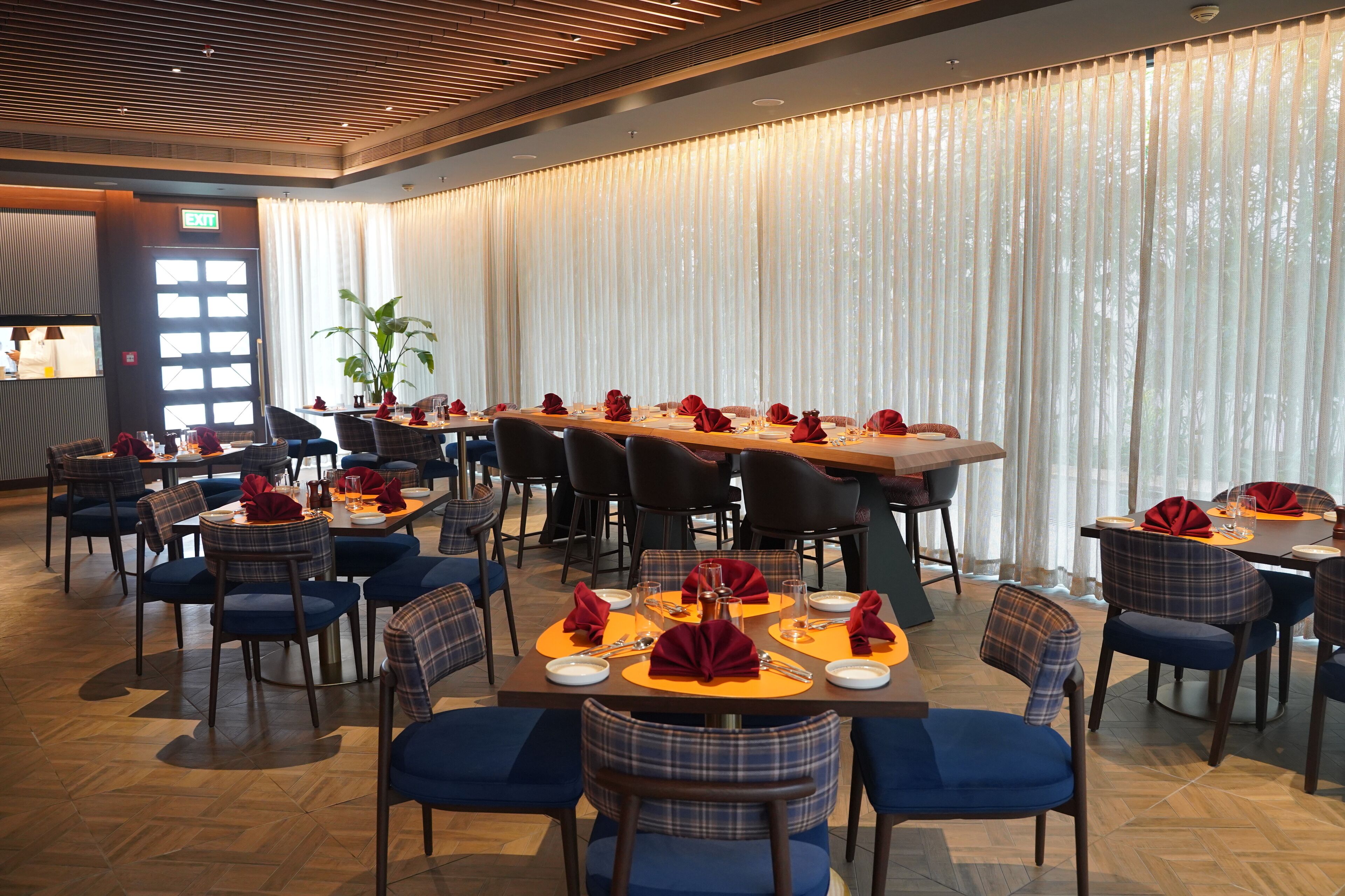 Un espace repas avec plusieurs tables dressées, doté de chaises à revêtement bleu et de serviettes rouges.