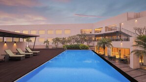Uma piscina com espreguiçadeiras e área coberta, cercada por um edifício com várias janelas e varandas.
