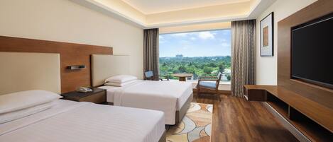 Habitación de hotel con dos camas, televisión, escritorio, silla y vista a la ciudad.