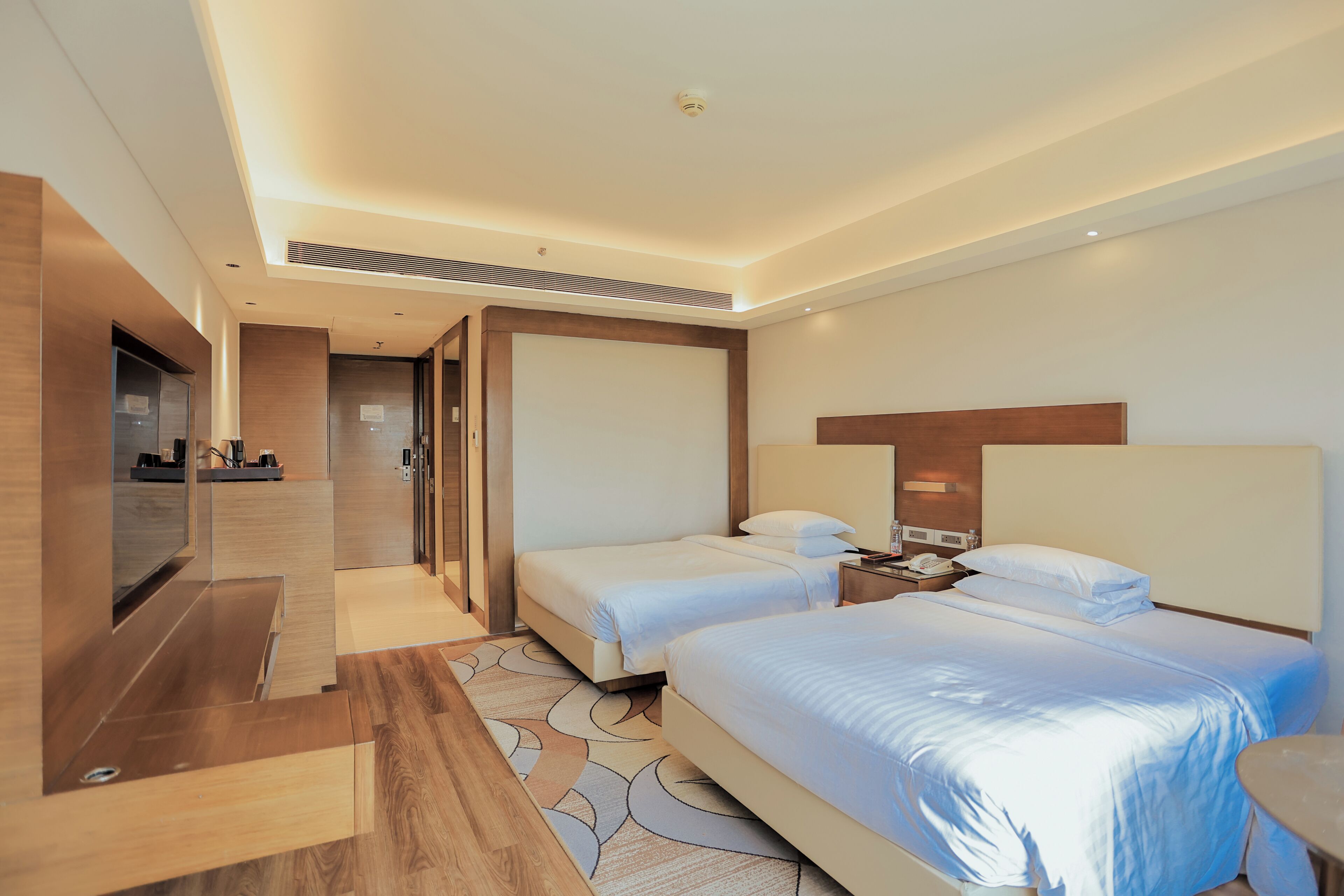 A hotel room with two beds, a TV, a desk, and a bathroom.