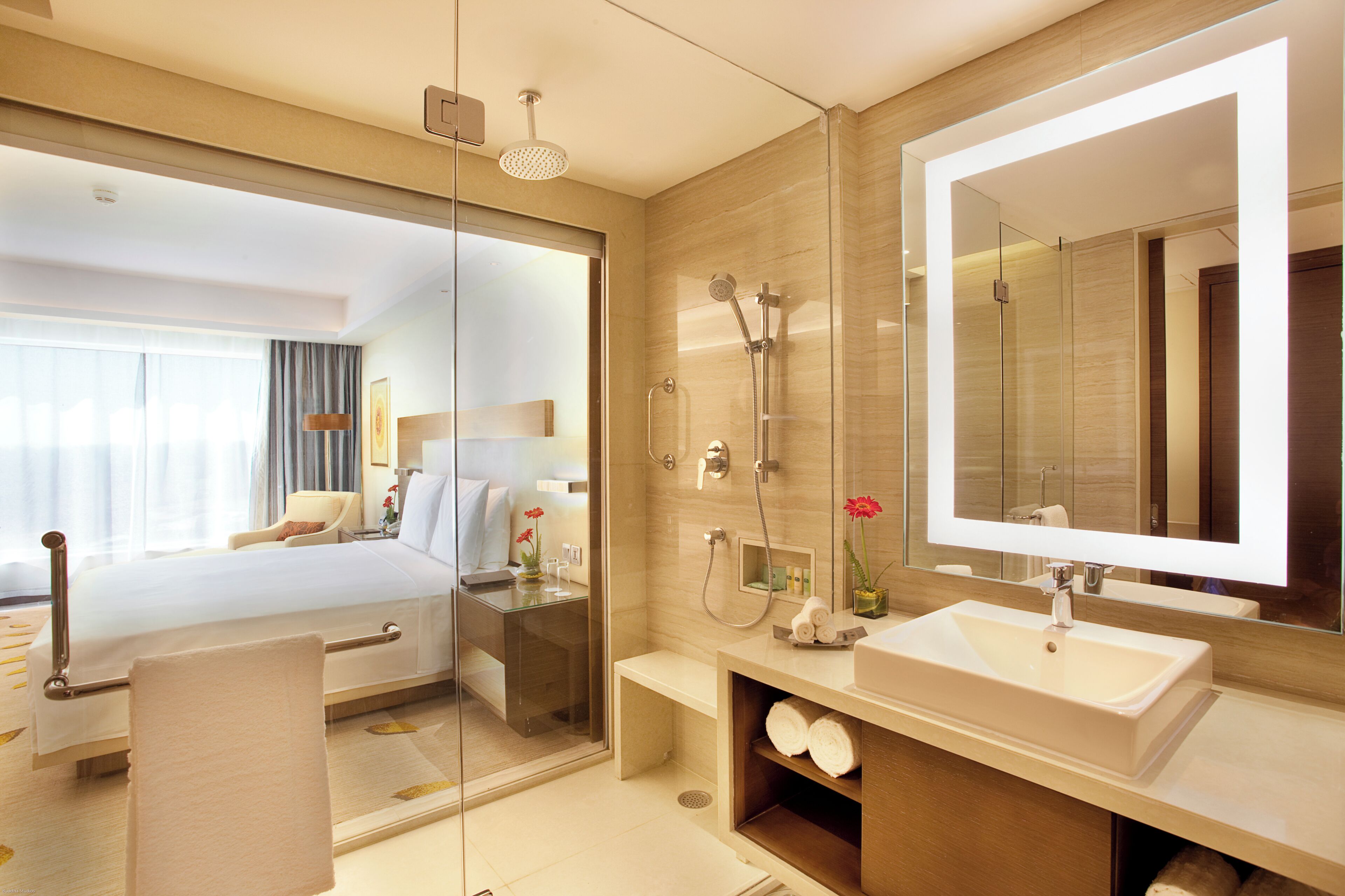 Une salle de bain d’hôtel moderne, dotée d’un grand miroir, d’un lavabo, d’une douche et d’un dressing ouvert délimité par des parois en verre.