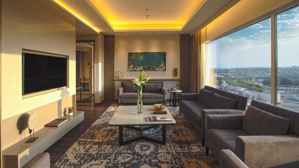Uma sala de estar moderna com televisão de tela plana, mesa de centro, sofás e uma grande janela com vista para a cidade.