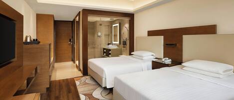 Habitación de hotel con dos camas, televisión, escritorio y zona de ducha.