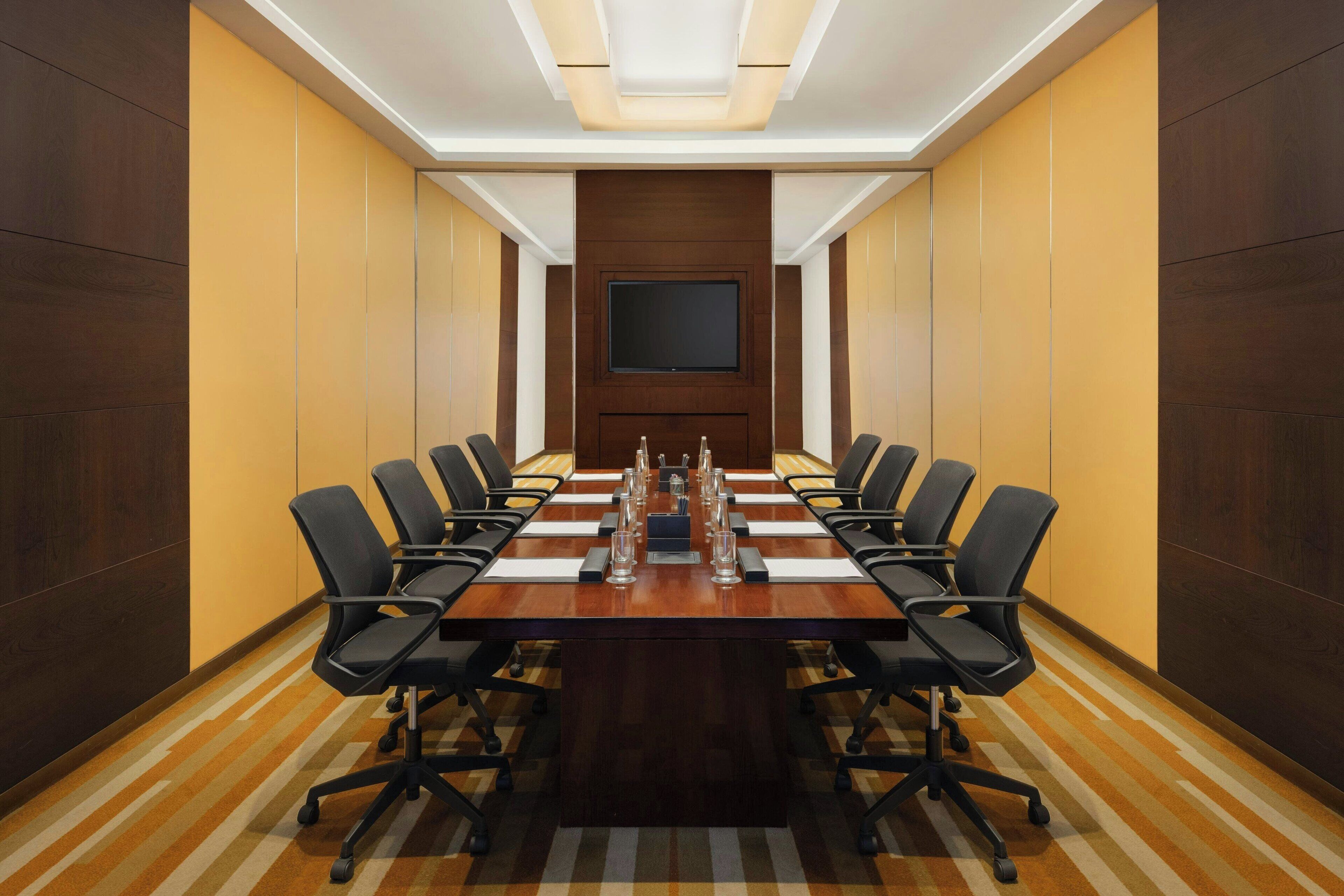 A conference room with a long table, chairs, a flat-screen TV, and a wooden accent wall.