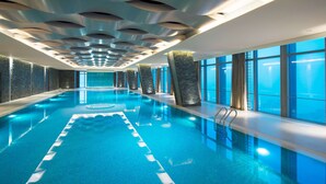 Una piscina interior con un diseño de techo moderno, pilares de piedra y grandes ventanales.