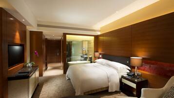 A hotel room with a bed, bedside table, lamp, TV, and a desk with a chair.
