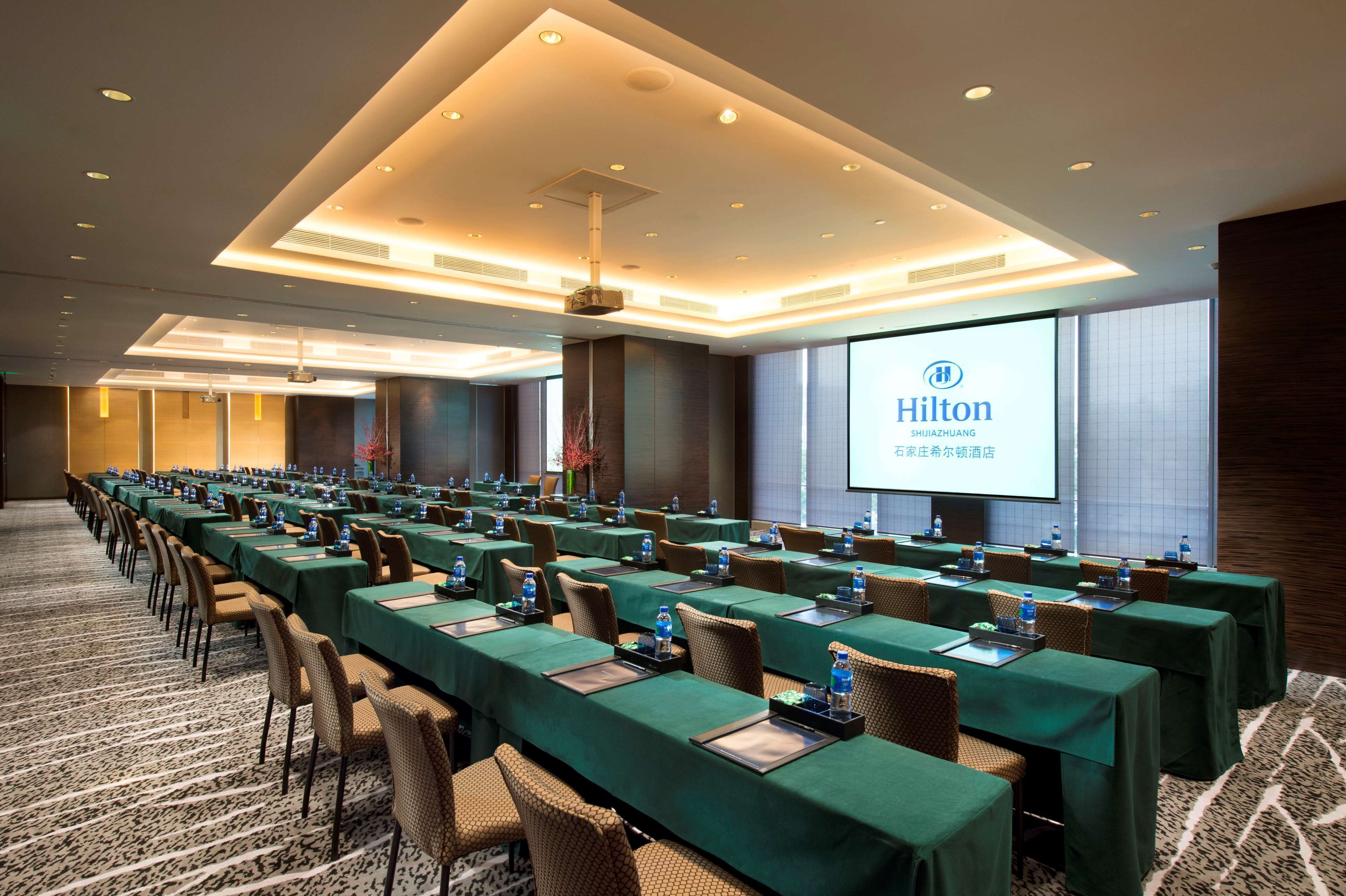 A conference room with long tables, chairs, and a projector screen displaying the Hilton logo.