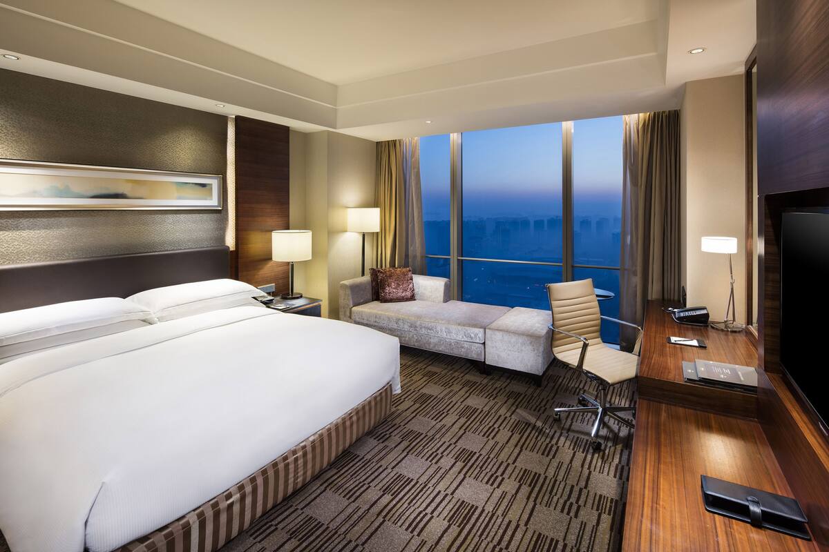 A hotel room with a large bed, a desk with a chair, a sofa, and a TV.