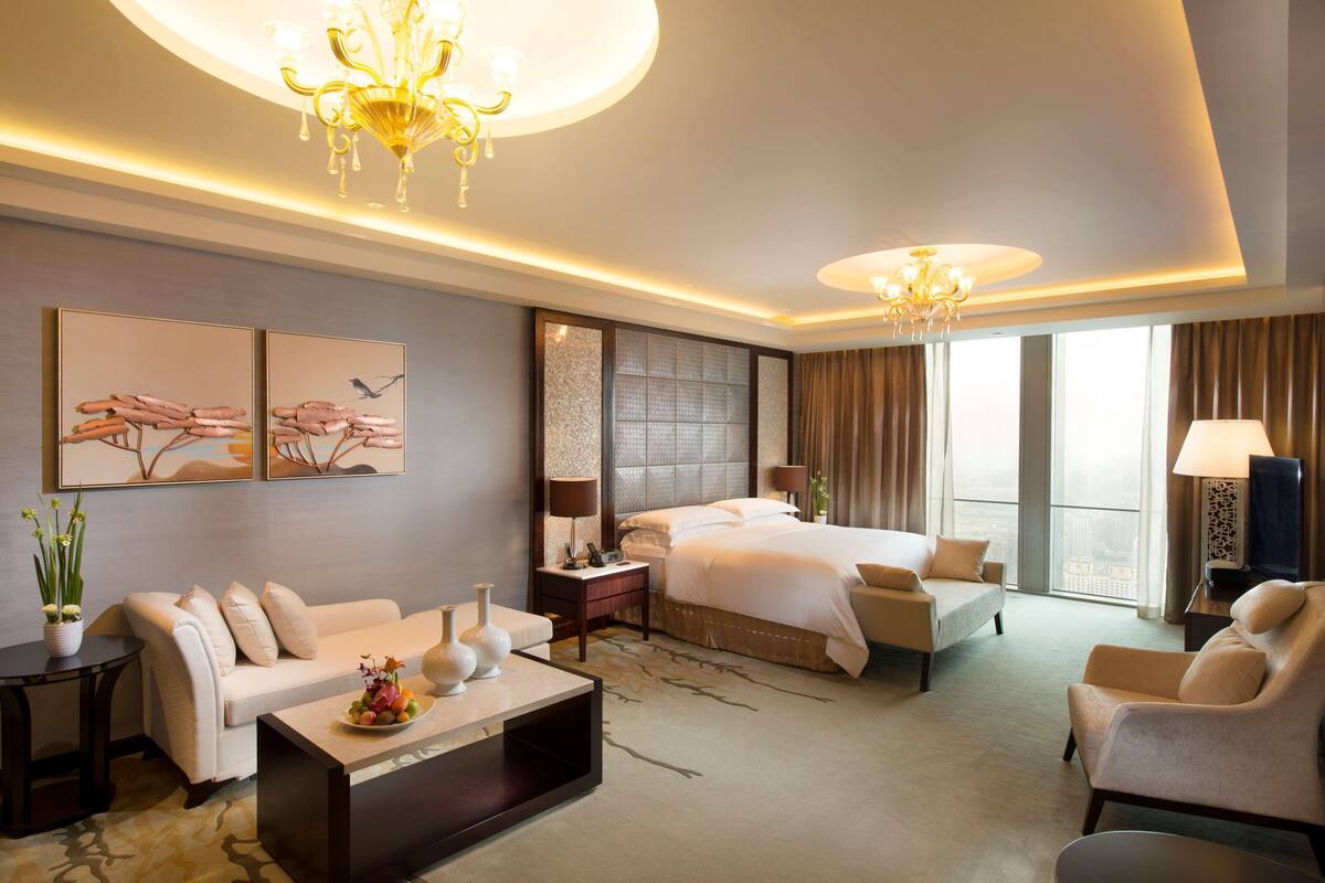 A modern hotel room with a large bed, a sofa, a coffee table, and a TV.