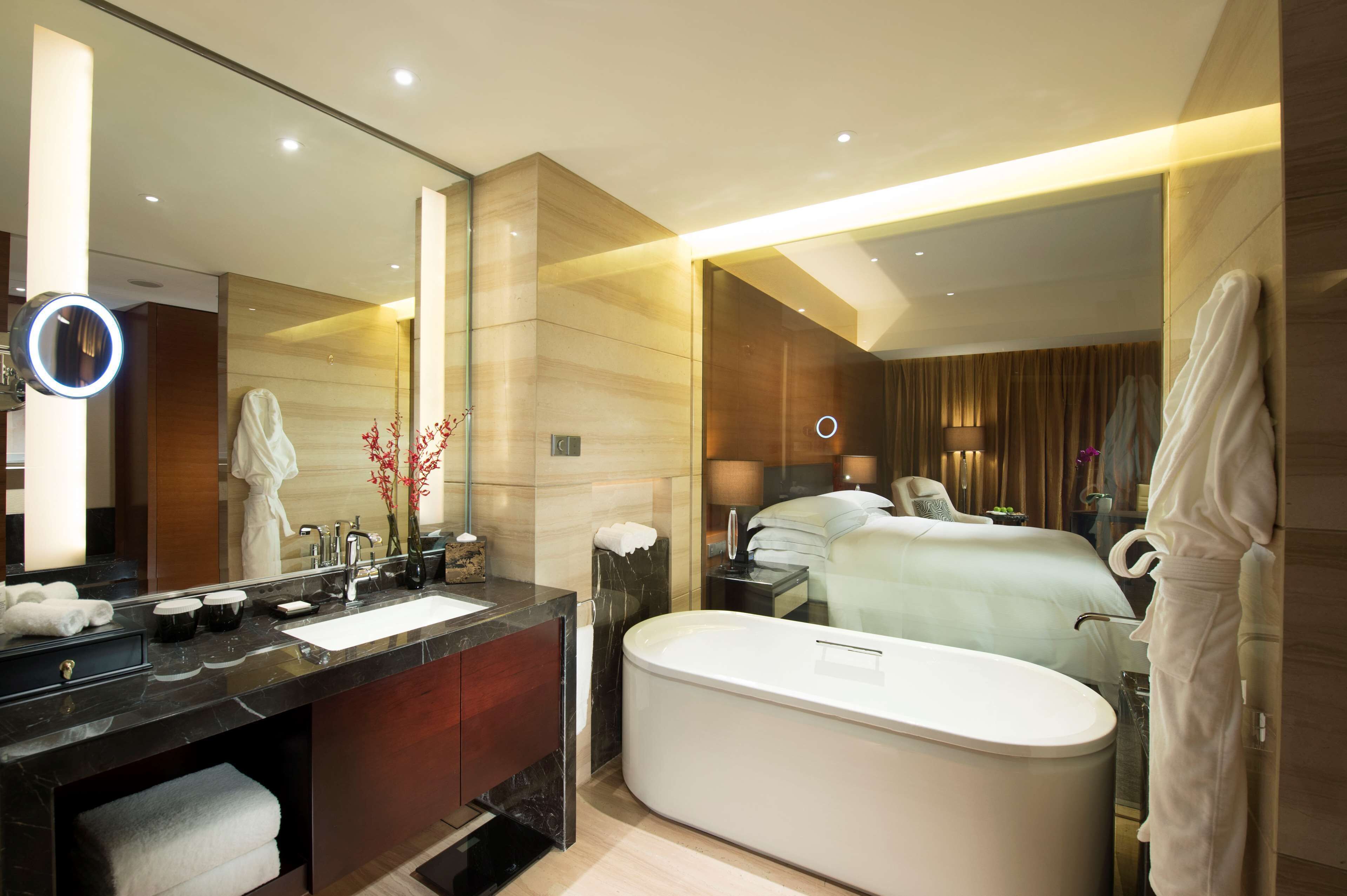 A modern hotel bathroom with a large mirror, a bathtub, a vanity with a sink, and a robe rack.