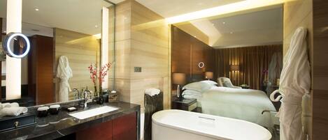 A modern hotel bathroom with a large mirror, a bathtub, a vanity with a sink, and a robe rack.