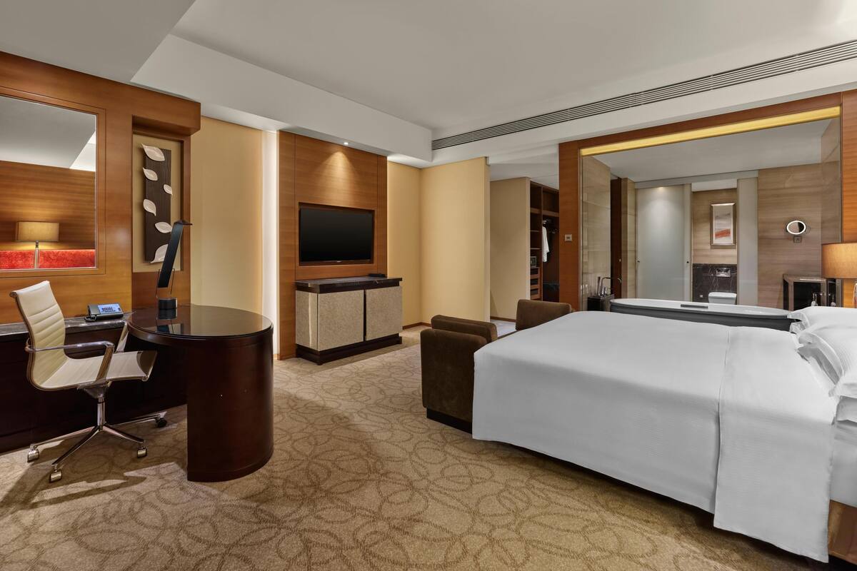 A hotel room with a bed, a desk with a chair, a television, and a bathroom with a mirror.