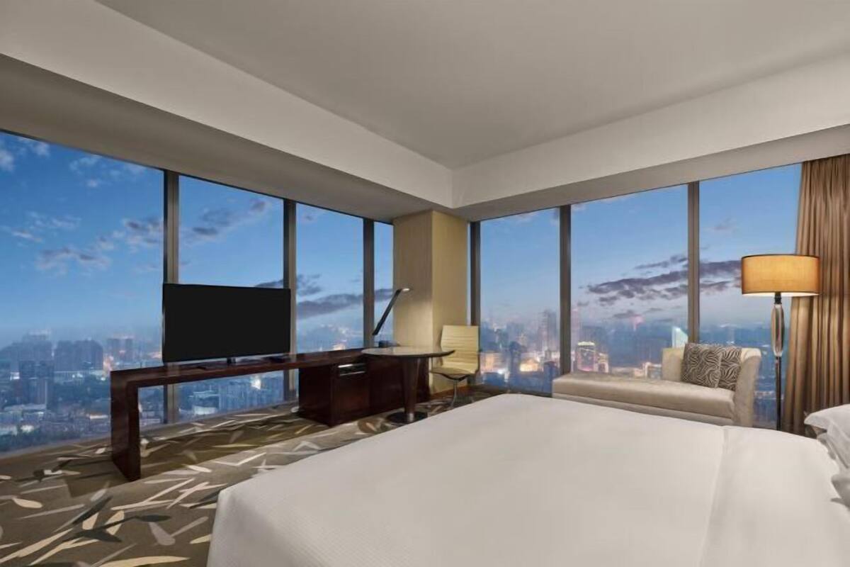 A hotel room with a large bed, a desk, a chair, a TV, and a city view.