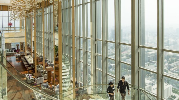 Un amplio atrio con piso de vidrio, un techo alto con lámpara decorativa y vistas de la ciudad a través de grandes ventanales.
