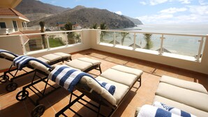 Un balcon avec des chaises longues, une vue sur la mer et une montagne en arrière-plan.