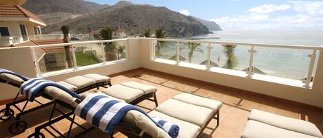 A balcony with sun loungers, a view of the sea, and a mountain in the background.