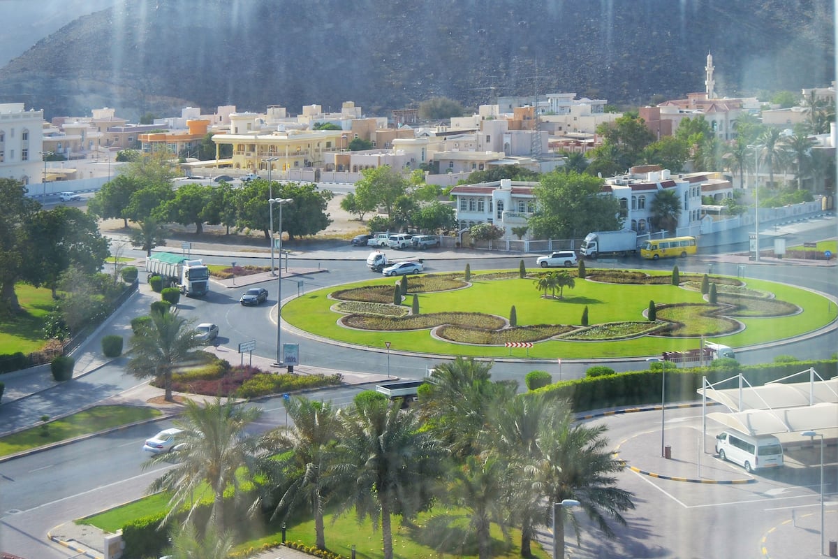 A roundabout with palm trees, a mosque, and residential buildings.