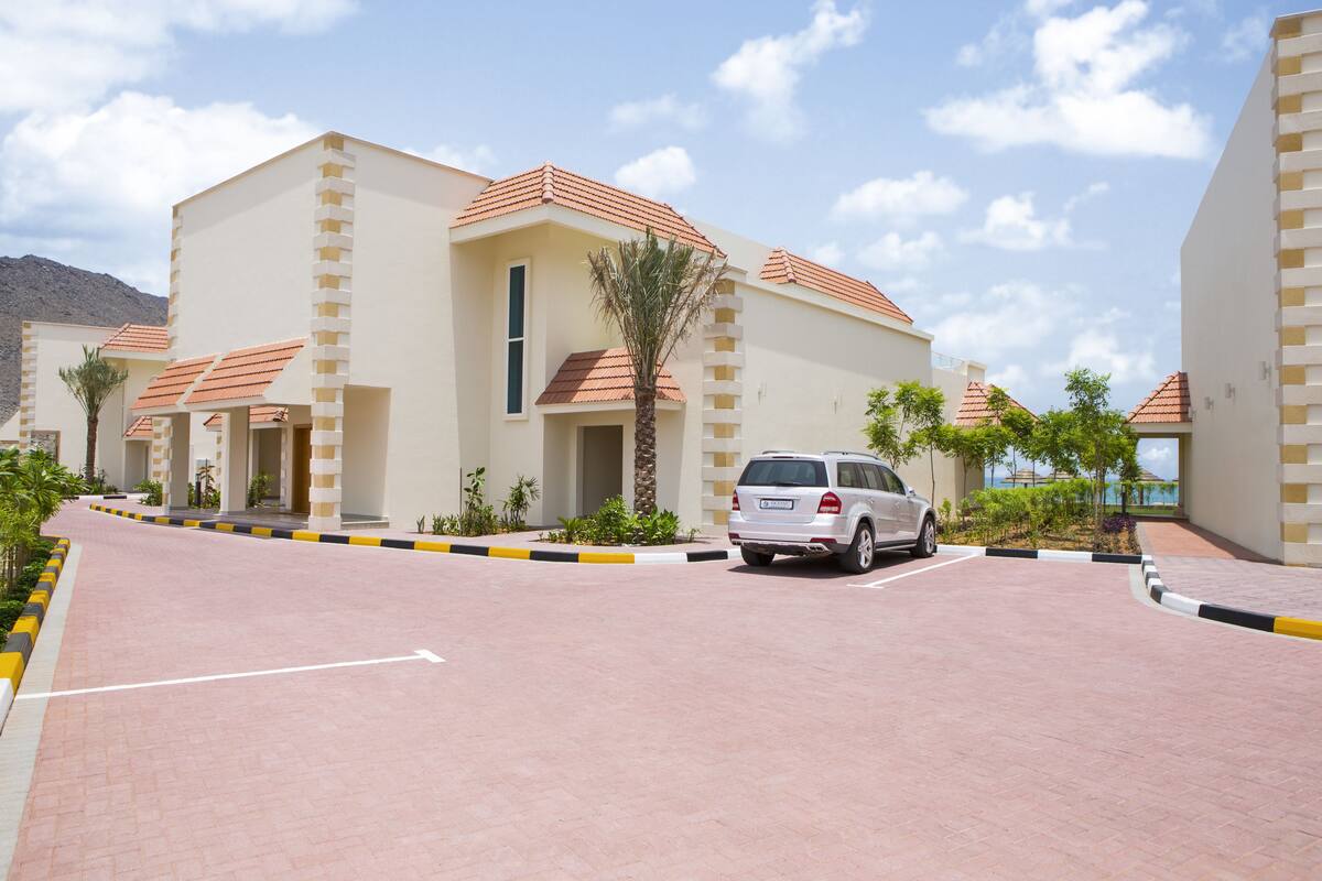 A modern hotel with a central entrance, a parking area, and a clear sky.