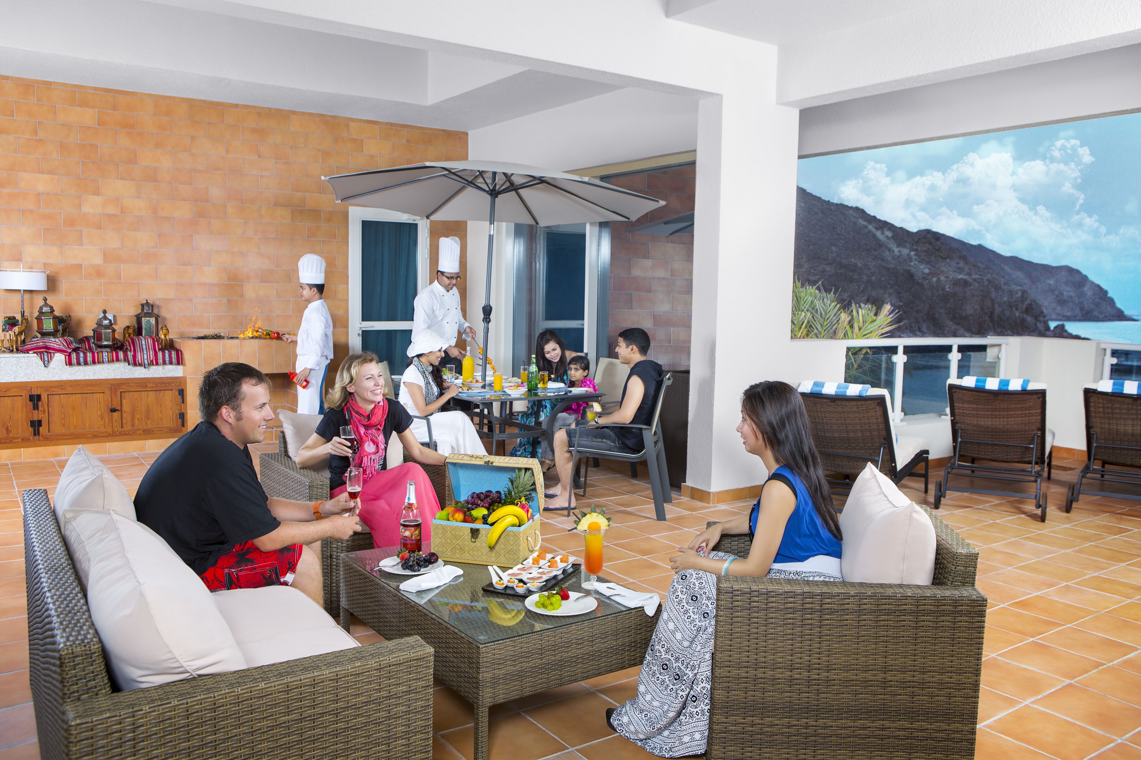 A dining area with wicker furniture, a chef, and guests enjoying a meal.