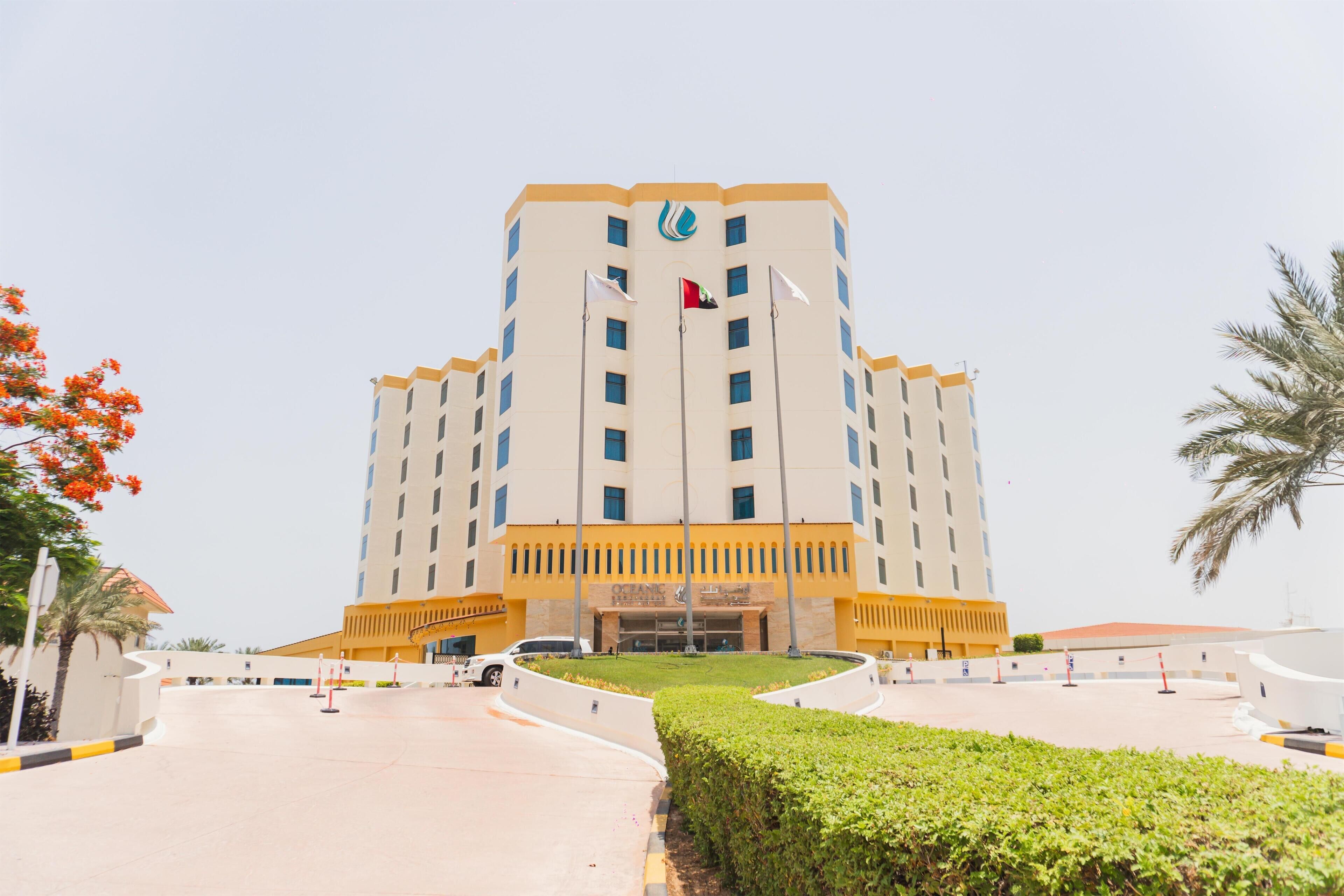 A multi-story hotel with a central entrance, flagpoles, and a landscaped courtyard.