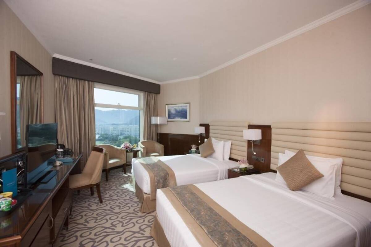 A hotel room with two beds, a desk, a TV, and a view of the city.