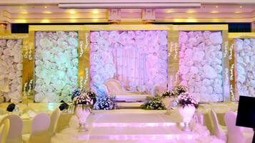Une salle de banquet dotée d’une scène centrale, de décorations florales blanches sur les murs et de tables dressées pour un événement formel.