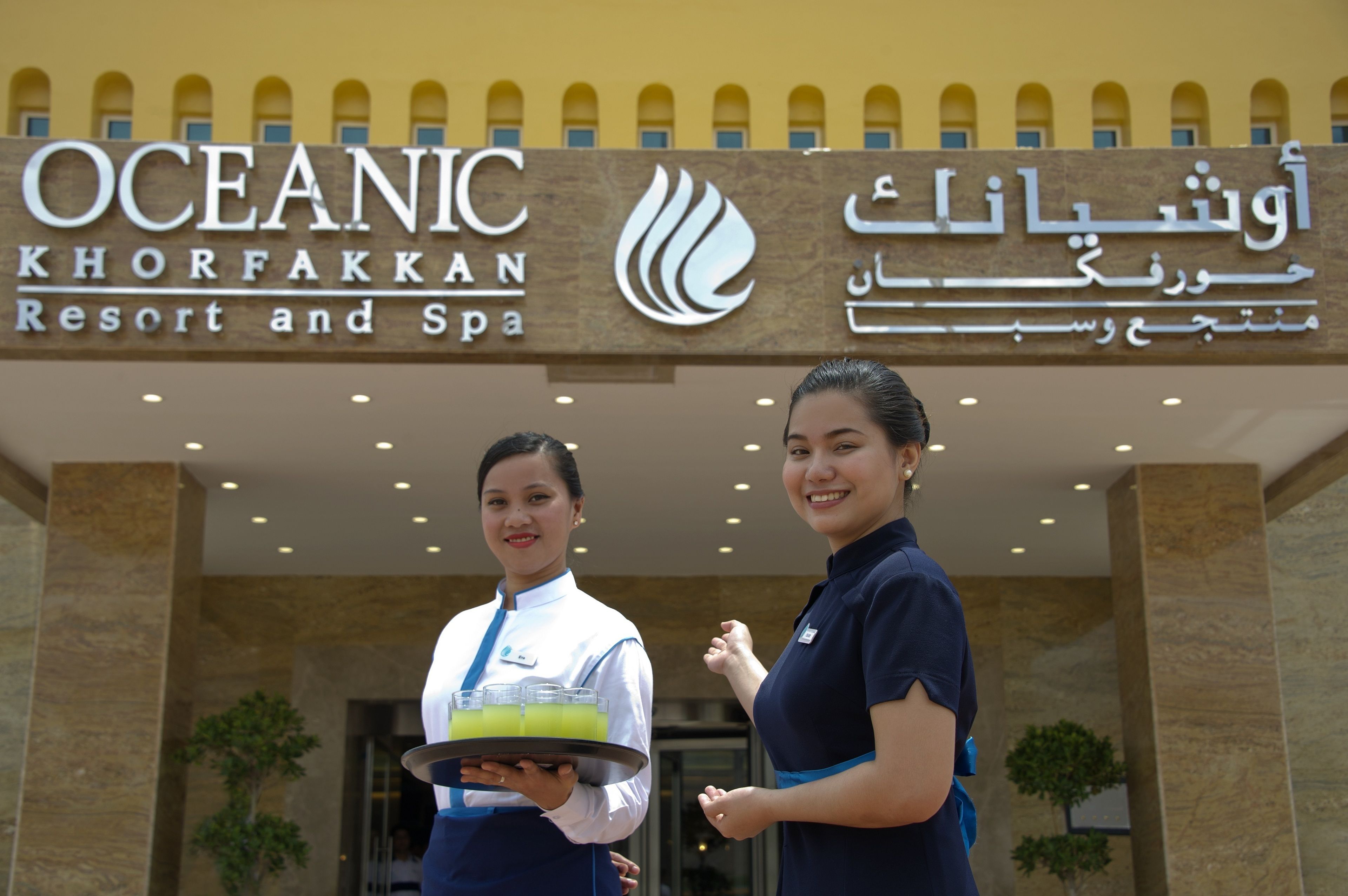 Placa do Oceanic Khorfakkan Resort and Spa com dois funcionários em frente.