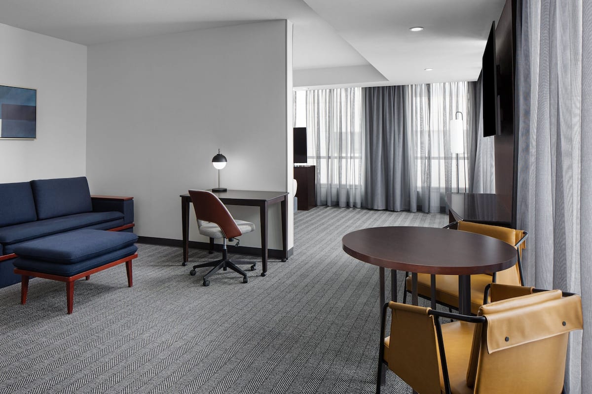 A hotel room with a sofa, a desk, a chair, a round table, and a TV.