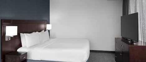 A hotel room with a large bed, a TV on a wooden cabinet, and a nightstand with a lamp.