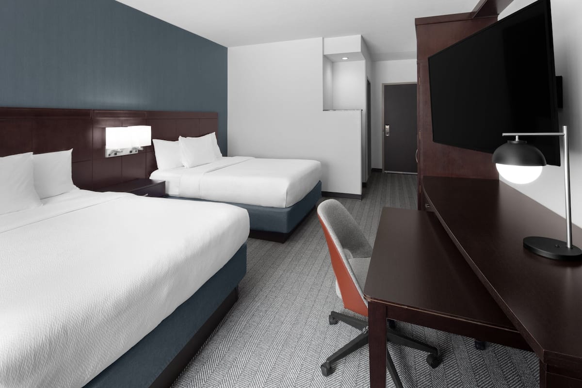 A hotel room with two beds, a desk, a chair, a TV, and a minibar.