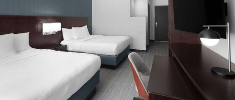 A hotel room with two beds, a desk, a chair, a TV, and a minibar.