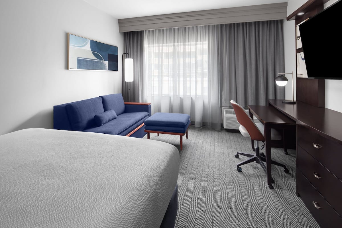A hotel room with a large bed, a sofa, a desk, and a TV.