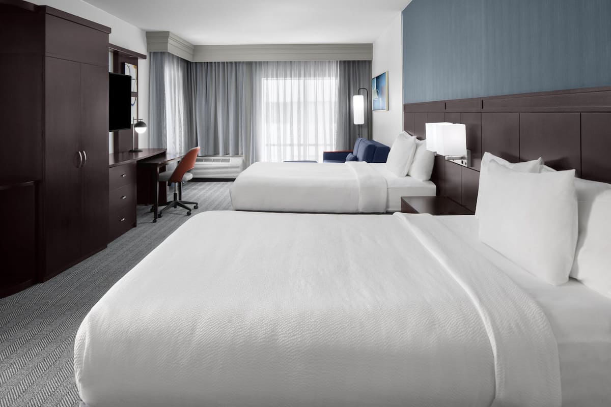 A hotel room with two beds, a desk, a chair, and a TV.
