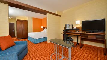 A hotel room with a bed, a desk with a computer, a television, and a sofa.