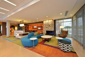 Un hall d’entrée moderne avec un canapé d’angle, des tables rondes, une cheminée et un mur décoratif en pierre.