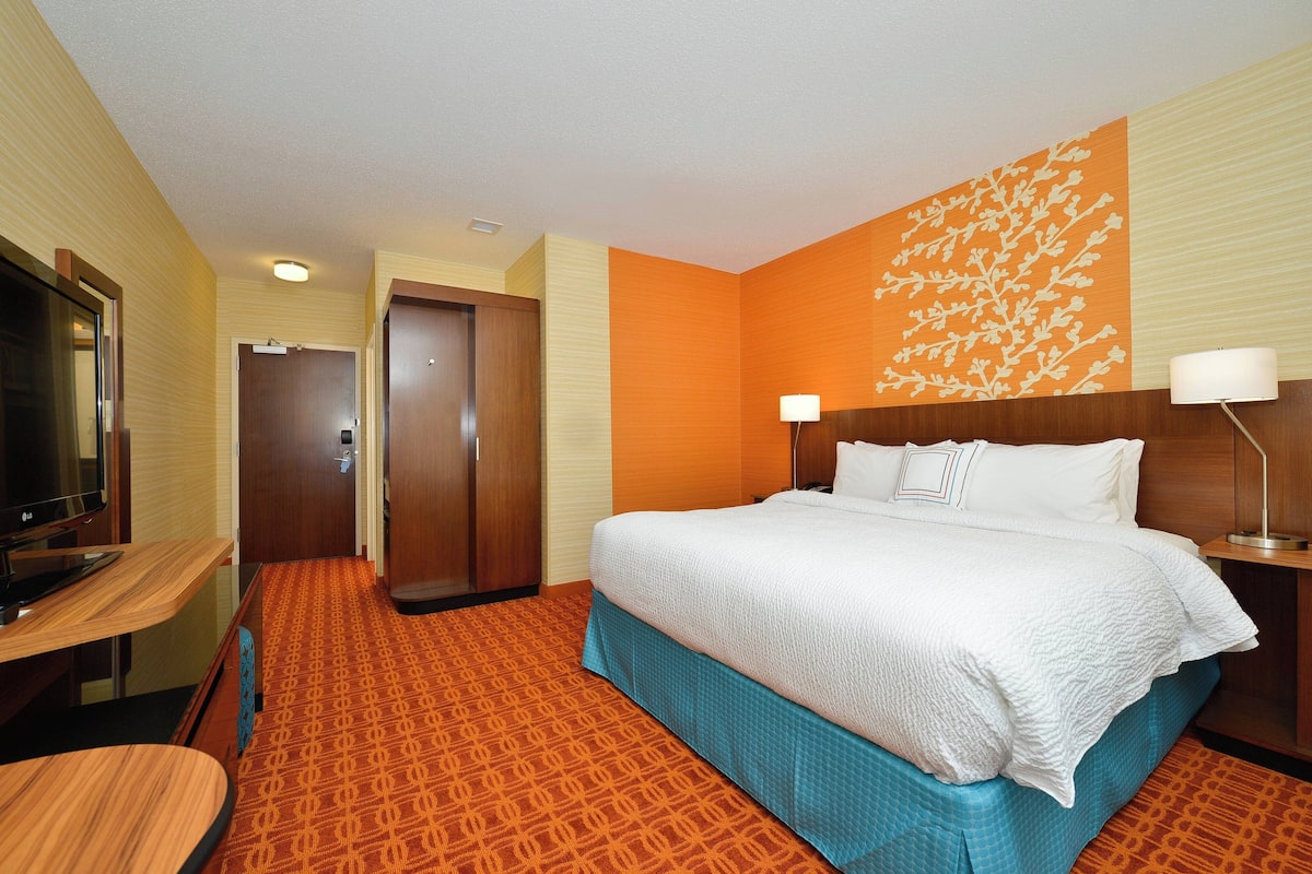 Une chambre d’hôtel avec un grand lit, une télévision, un bureau et une moquette à motifs.