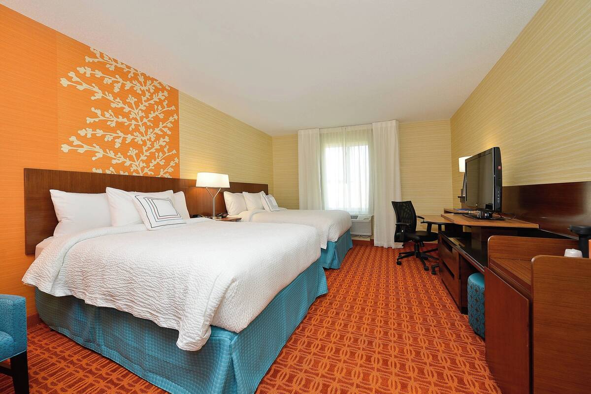 Une chambre d’h ôtel avec deux lits, un bureau, une télévision et une moquette à motifs.
