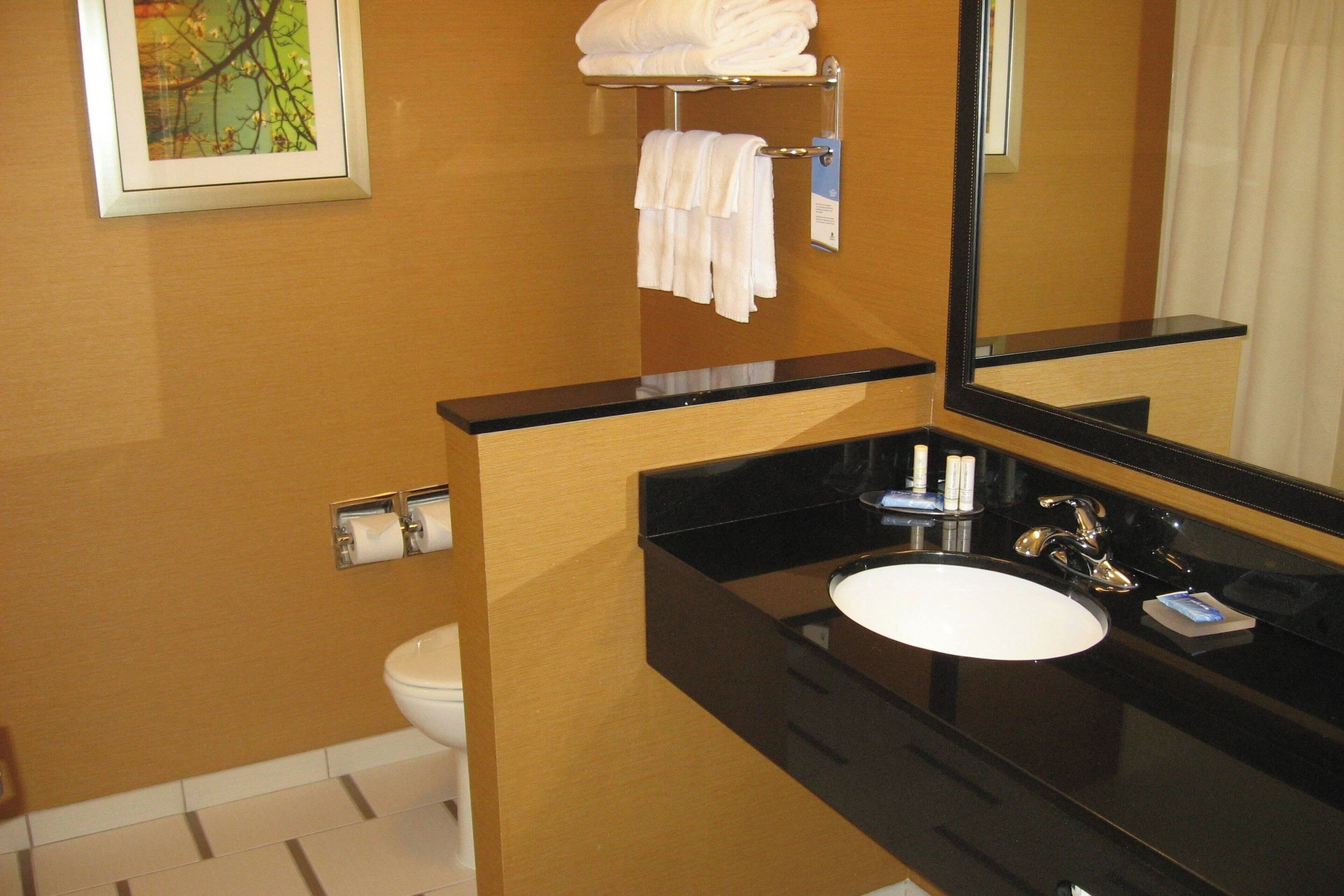 A bathroom with a black countertop, white sink, and a mirror. There is a towel rack with folded towels above the sink.