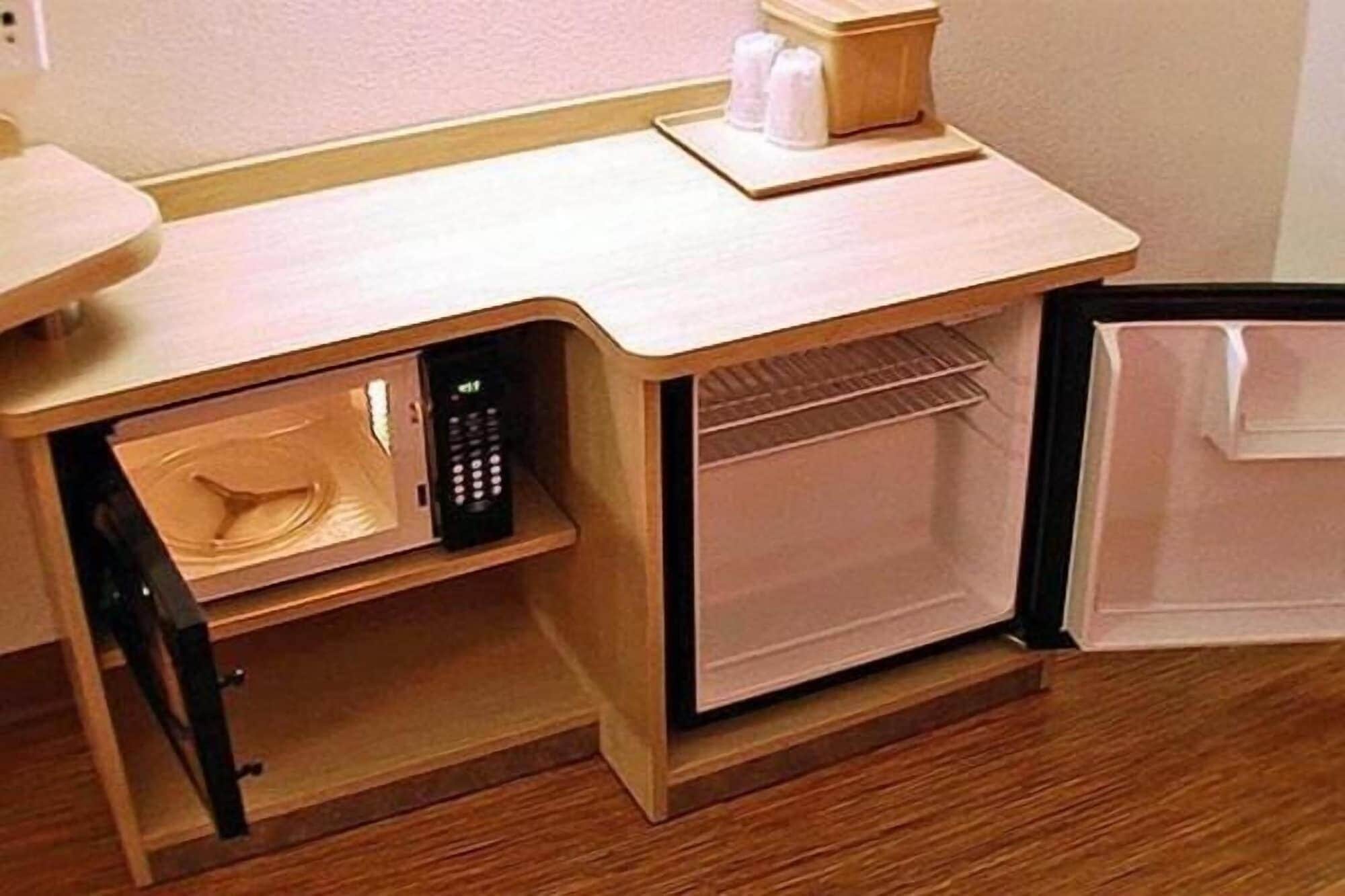 A compact kitchen with a microwave, a small refrigerator, and a wooden cabinet.